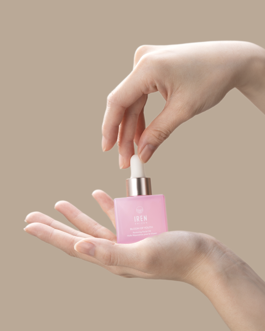 A woman's hand holding a small bottle of BLOOM OF YOUTH Restoring Facial Oil, a customized Japanese skincare product by IREN Shizen. #all-groups