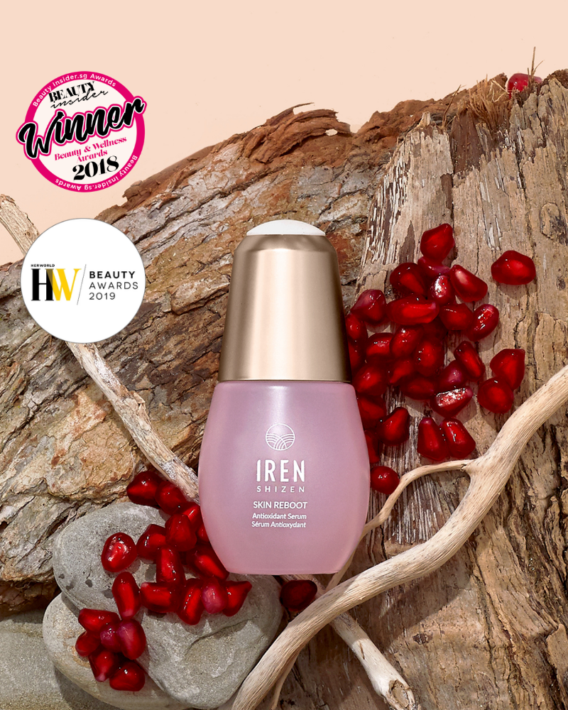 A bottle of IREN Shizen SKIN REBOOT Antioxidant Serum is shown on wood with pomegranate seeds, next to two award badges from 2018 and 2019.