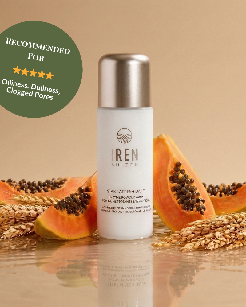 A bottle of START AFRESH DAILY Enzyme Powder Wash by IREN Shizen, a gentle daily exfoliator, is shown with papaya slices and wheat stalks, featuring a green badge recommending it for oiliness, dullness, and clogged pores.