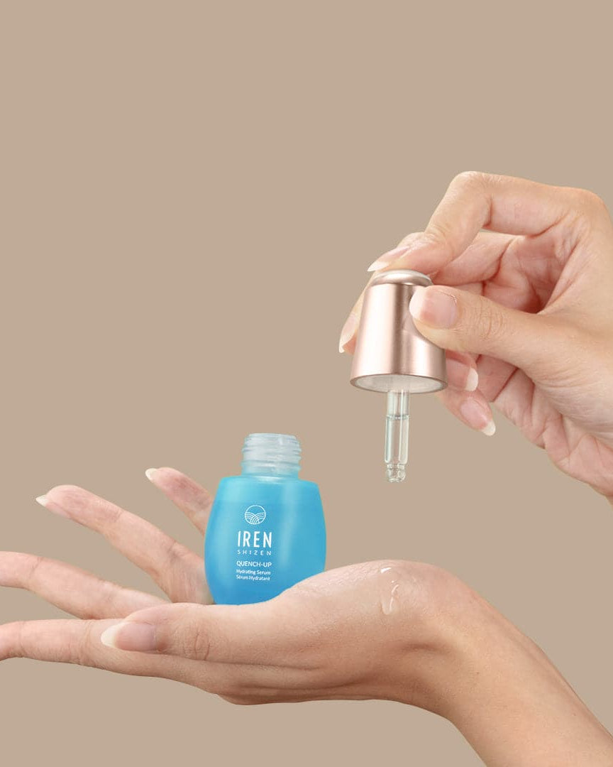 A woman's hand holding a bottle of custom Japanese skincare, the QUENCH-UP Hydrating Serum by IREN Shizen.