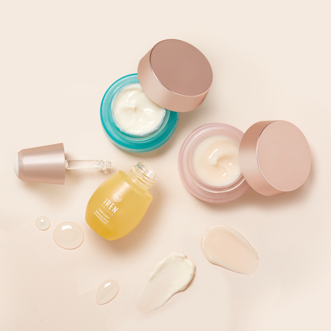 The MOCHI SKIN Instant Glow Travel Set by Fast Bundle includes two open jars and a dropper bottle of skincare creams and serum, elegantly displayed with drops and smears on a light background.