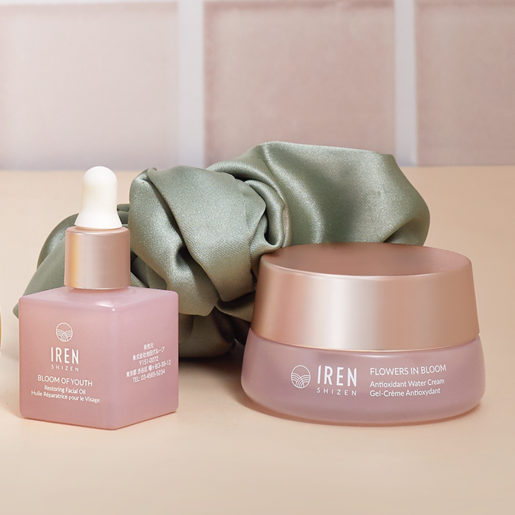 An arrangement of the IRÉN Shizen AFTER SUN Repair Routine, including a bottle of Bloom of Youth Magnetic Peel Off and a jar of Flowers in Bloom Antioxidant Water Cream, ideal for your after-sun routine, placed beside a green hair scrunchie.