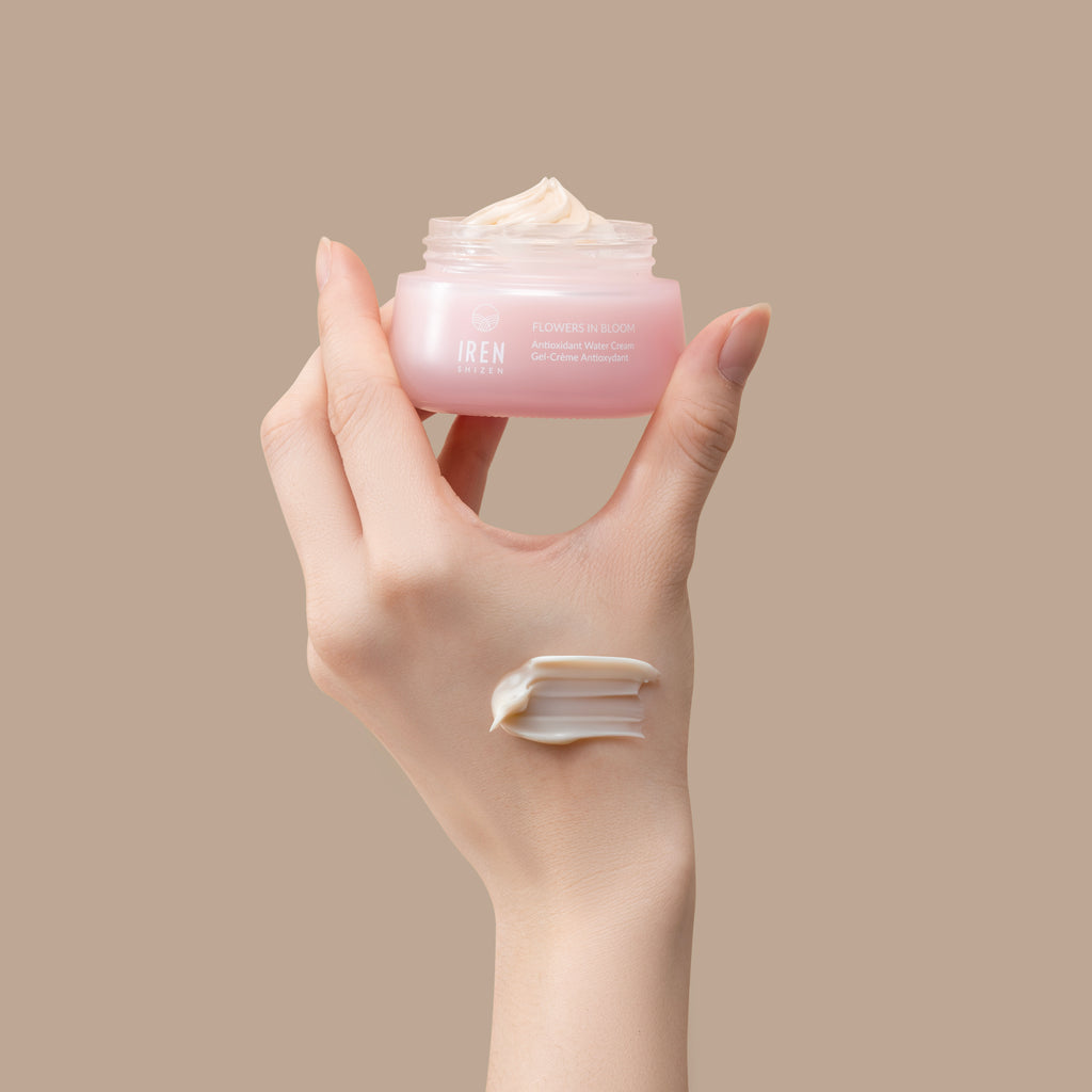 A hand holds an open jar of AFTER SUN Repair Routine by IREN Shizen. A dollop of the antioxidant water cream is applied to the back of the hand.