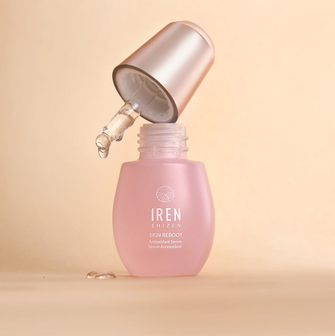 A pink bottle of the PINK OCTOBER Skincare Set's IRÉN Shizen Skin Reboot Antioxidant Serum, featuring a silver dropper cap dispensing a drop of serum, supporting Breast Cancer Awareness.