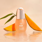 A bottle of custom Japanese skincare, IREN Shizen GLOW-GETTER Renewal Serum, next to a slice of mango.